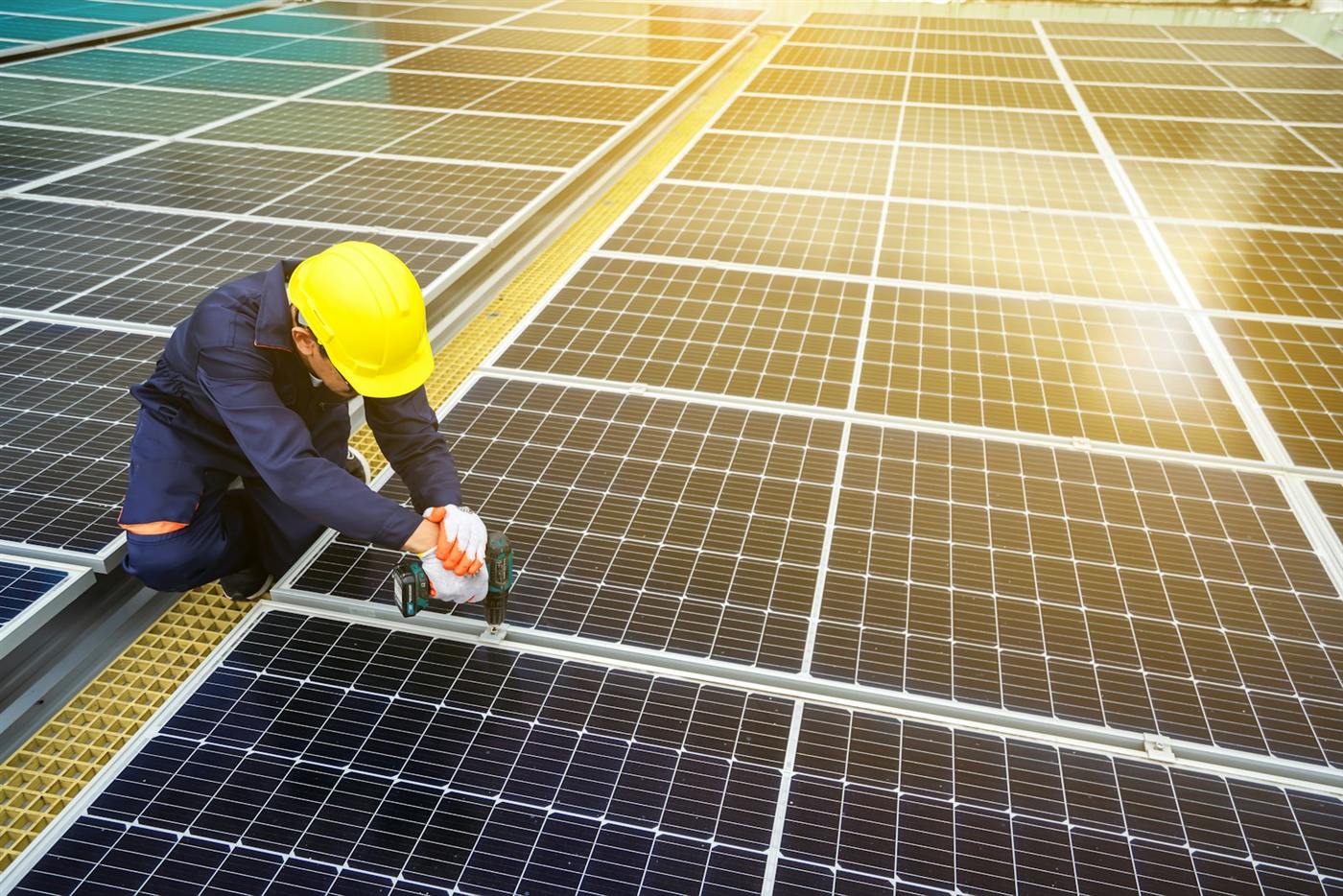 Installer in a yellow helmet fixing a solar module on a large array