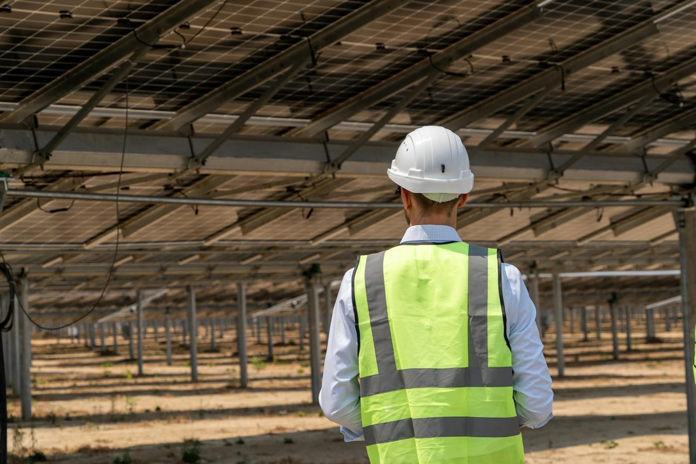 Engineer in a safety vest and helmet inspecting a ground-mounted solar plant