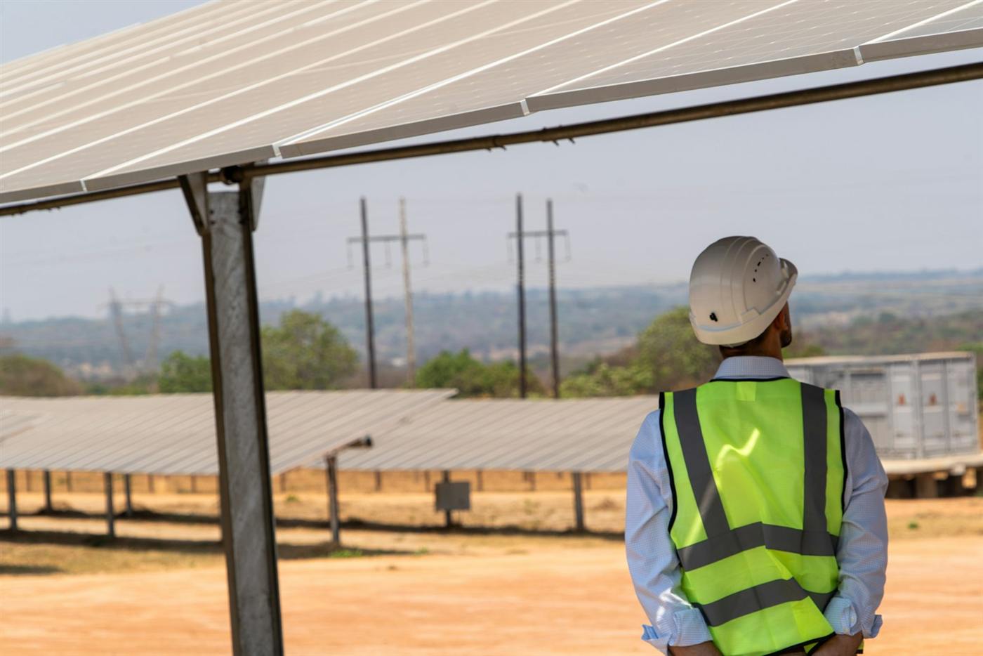 Engineer in a safety vest and helmet surveying a ground-mounted solar site